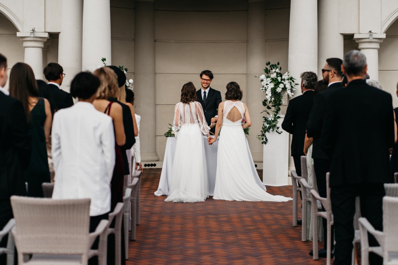 Image of wedding ceremony with guests on the side of the aisle, two people getting married and an officiant.