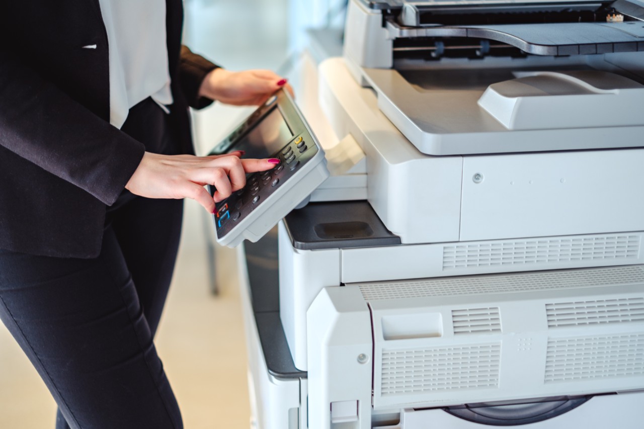 A person stands by a copy machine, with one hand pressing a button on the menu