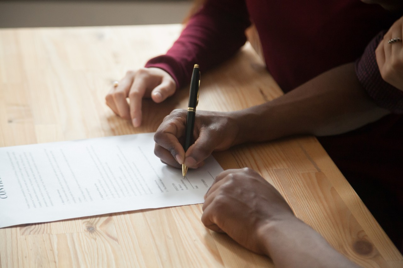 Two people sit next two each other, while one signs a document